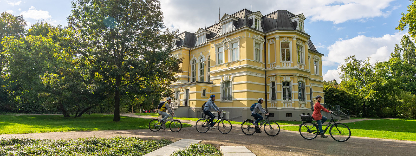 Niederrhein Fahrradfahrer vor Museum Vier Fahradfahrer*innen fahren vor einem Museumsgebäude entlang